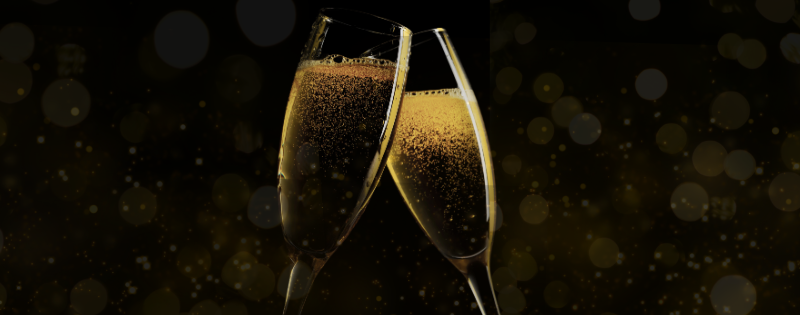 Two glasses of sparkling wine raised in a toast against a dark background.